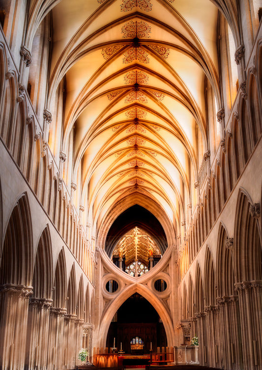 Golden vaulted arches of Wells Cathedral glowing in warm light, with a central view of the chancel and cross.
