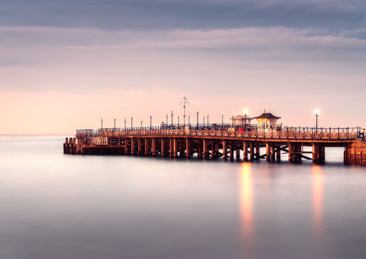 Long exposure photograph of Swanage Pier at twilight with soft reflections in the sea and glowing lamps.